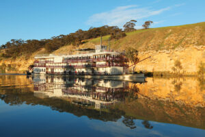 PS Murray Princess paddlewheeler reflected on the still waters of the Murray River near golden cliffs.