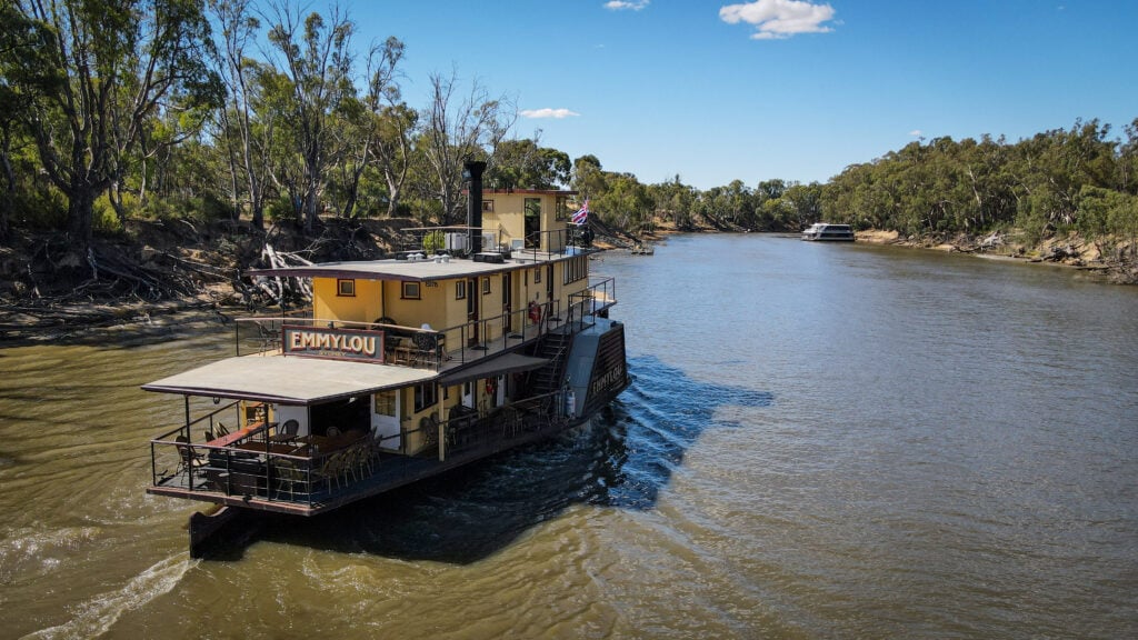 Paddle steamer Emmylou cruising the Murray River under clear blue skies, with forested riverbanks on either side.